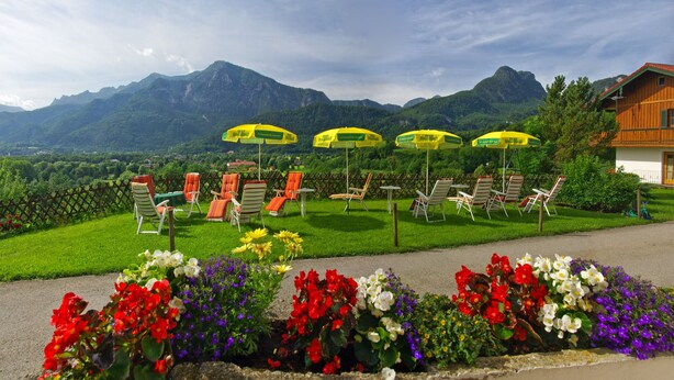 A garden with colorful flowers, outdoor seating, and a mountain backdrop. - Leitnerhof (Bad Reichenhall)