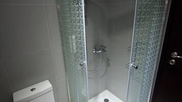 A bathroom with a glass-enclosed shower, a toilet, and tiled walls.