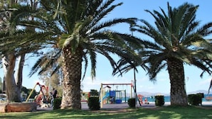 Un parc avec des palmiers, une aire de jeux et une vue sur la mer.