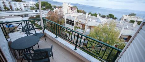 A balcony with a table and chairs, overlooking a cityscape and the sea.