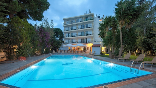 Une piscine entourée d’arbres et d’un b âtiment doté de balcons, avec des chaises longues et des parasols à proximité.