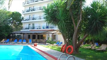 A pool area with lounge chairs, a building with balconies, and a tree.