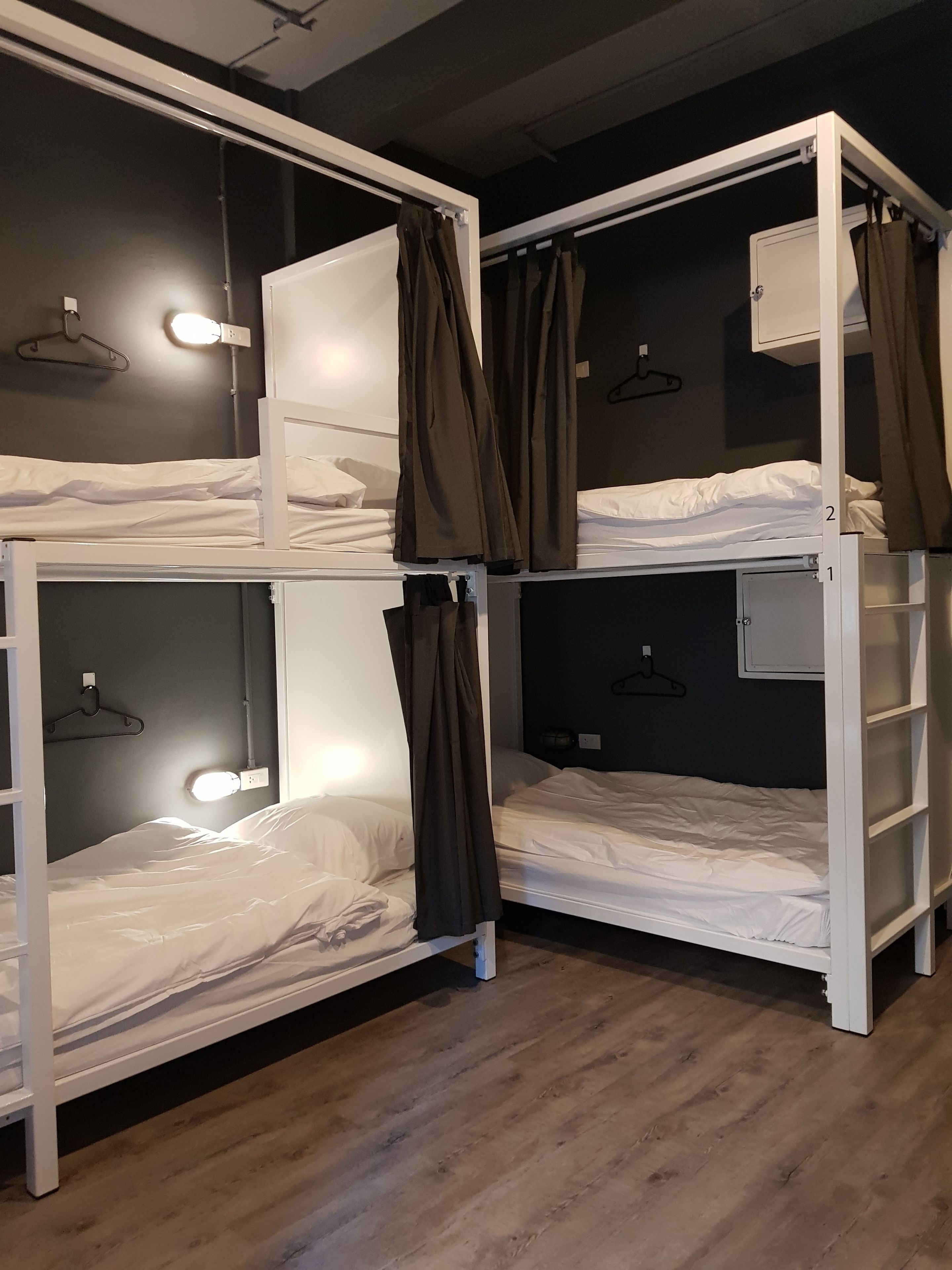 Une chambre avec des lits superposés, des montures blanches, des rideaux marron et un plancher en bois.