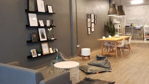 A modern living room with a grey sofa, a round coffee table, and a dining area with a wooden table and chairs. - The Cocoon Hostel (Bangkok)