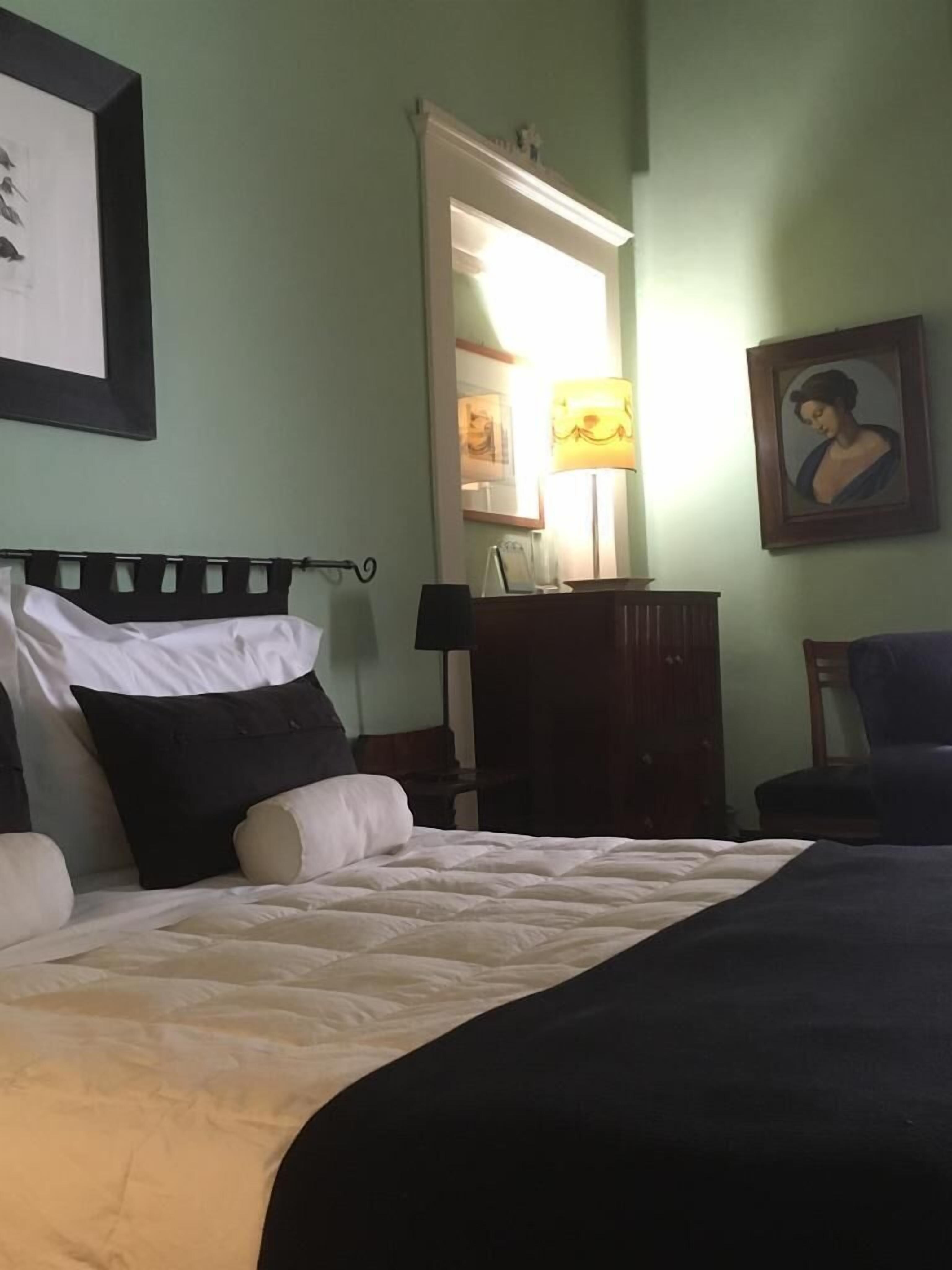 A neatly made bed with a black and white duvet, a wooden nightstand with a lamp, a wooden dresser, and a framed portrait on the wall.