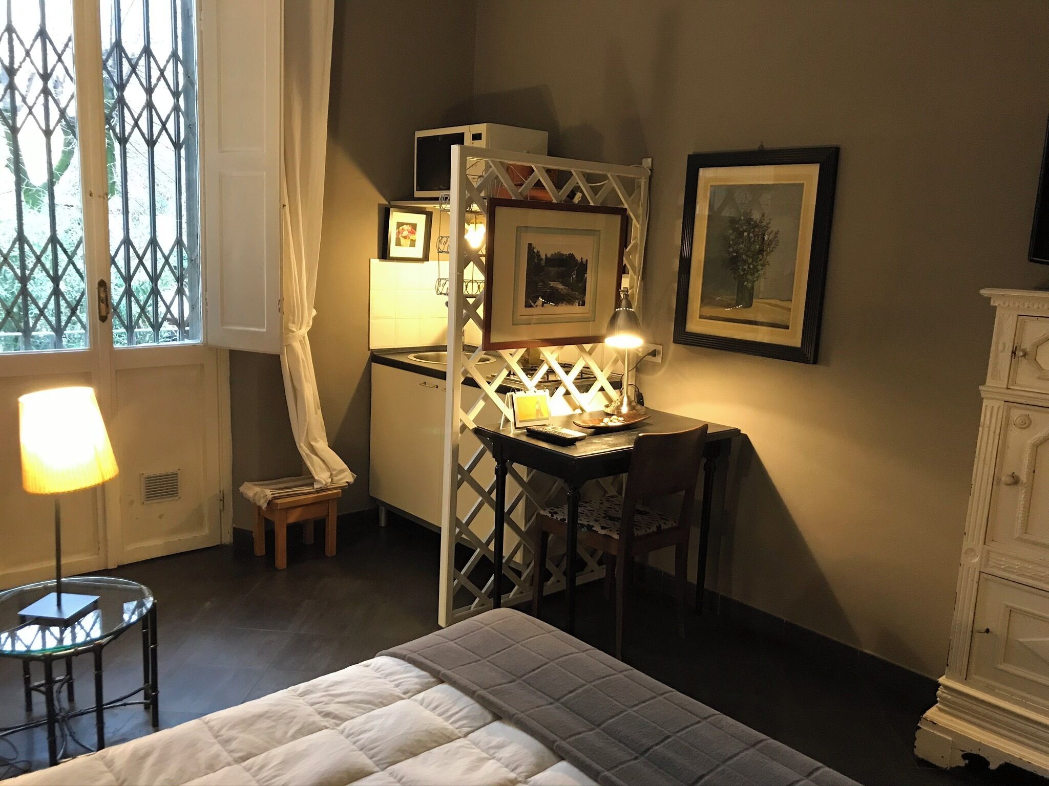 A bedroom with a bed, a desk with a lamp, a chair, a dresser, and a window with curtains.