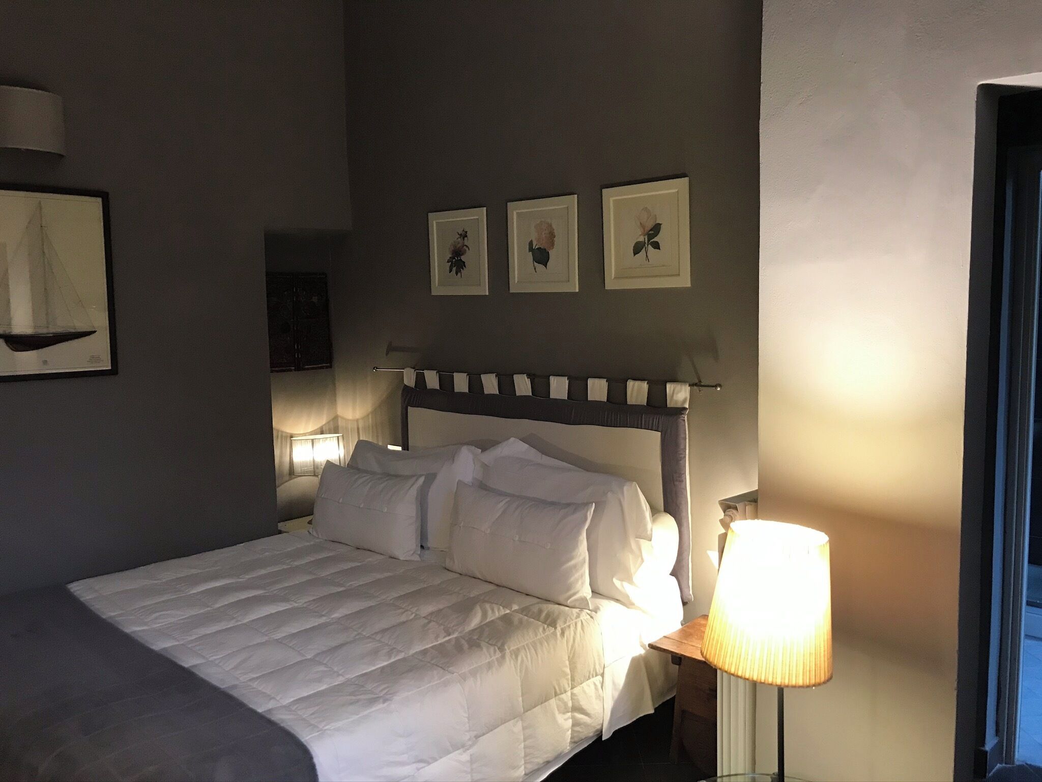 A neatly made bed with white bedding, a bedside lamp, and three framed pictures on the wall.