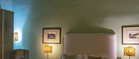 A hotel room with a bed, two chairs, a table, and framed pictures on the walls.