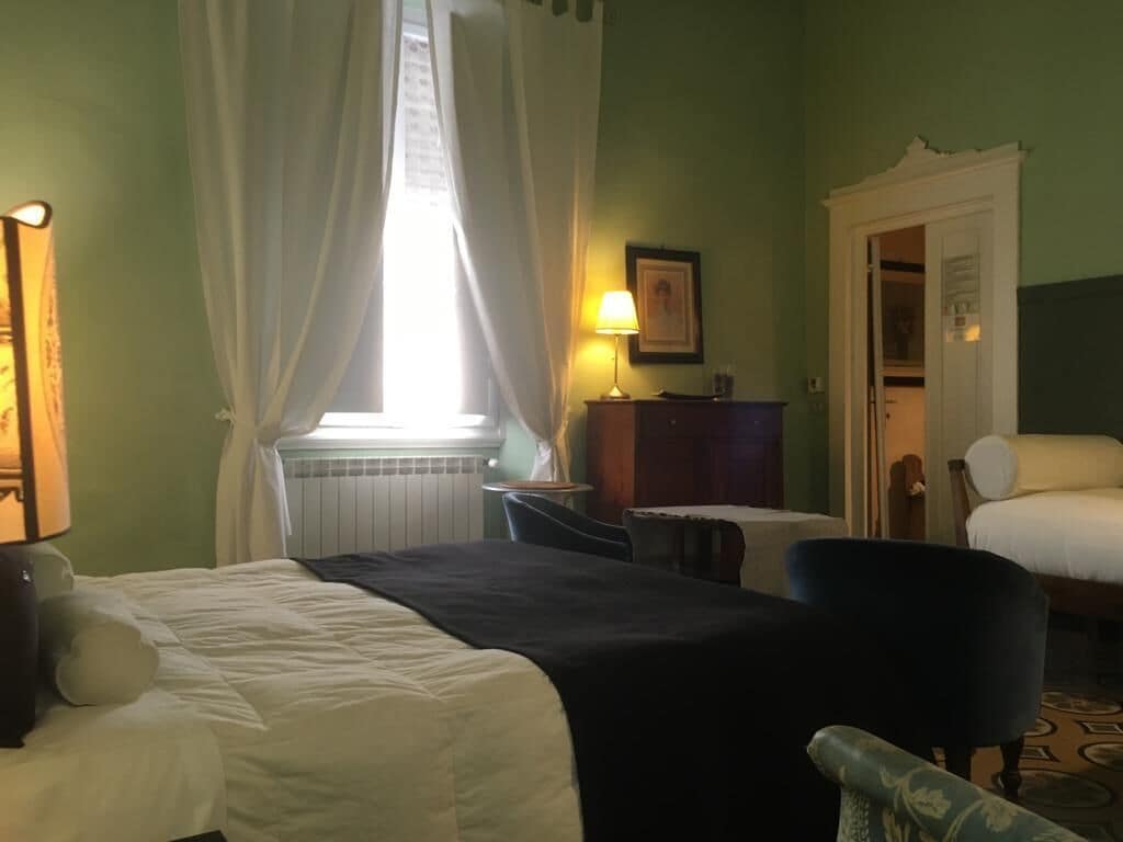 A hotel room with a bed, a chair, a desk, and a lamp.