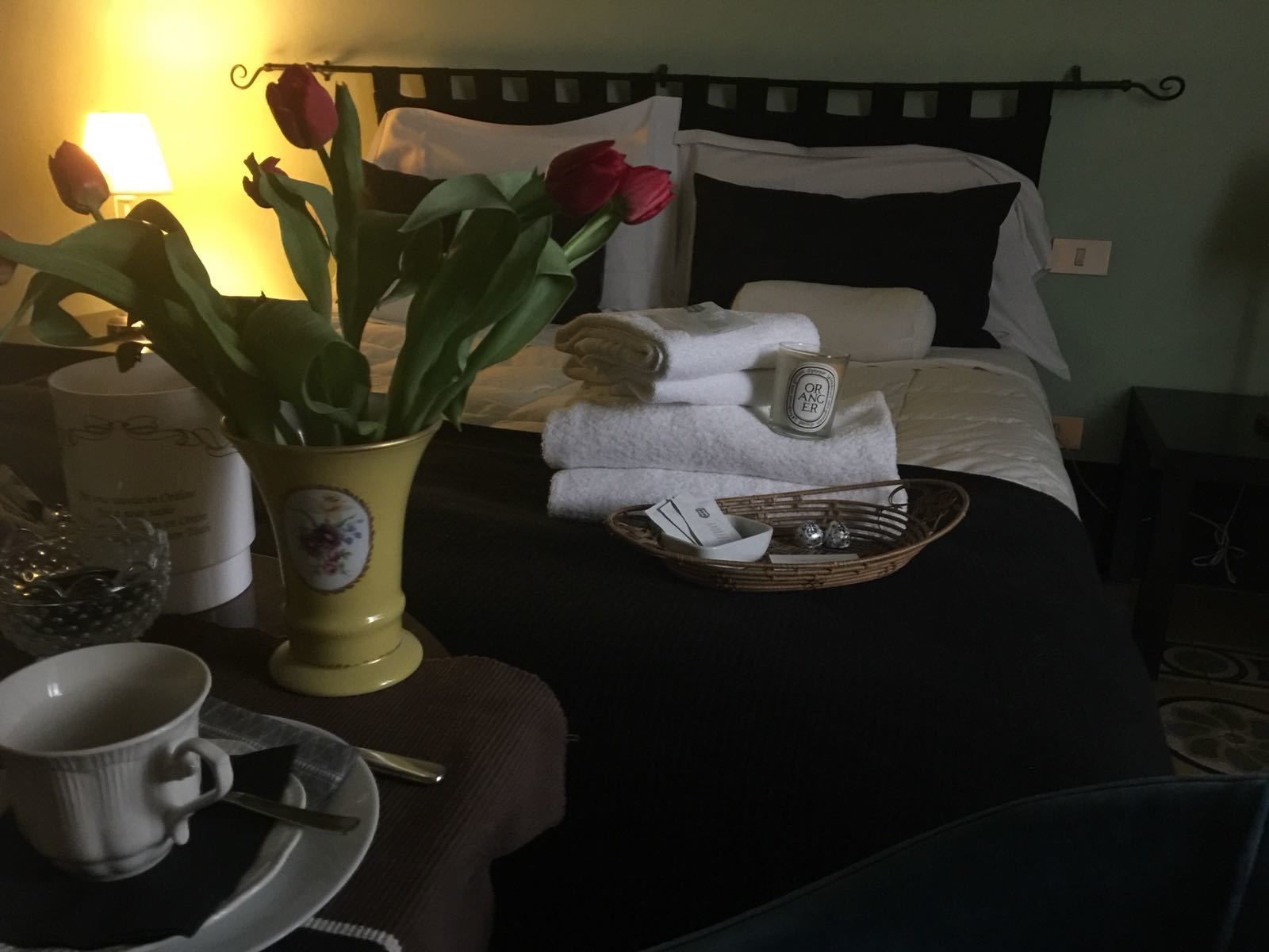 A neatly made bed with white and black bedding, a vase with red tulips, a candle, and a tray with a cup and a spoon on a bedside table.