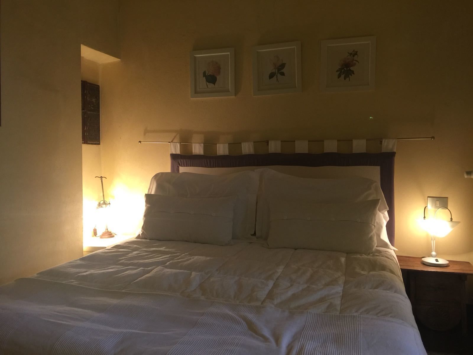 A neatly made bed with white linens, a headboard with a striped pattern, and three framed pictures on the wall above.