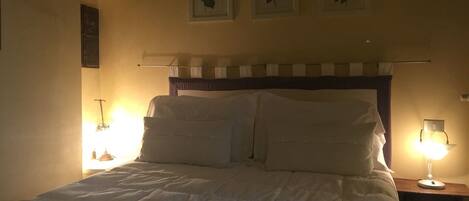 A neatly made bed with white linens, a headboard with a striped pattern, and three framed pictures on the wall above.