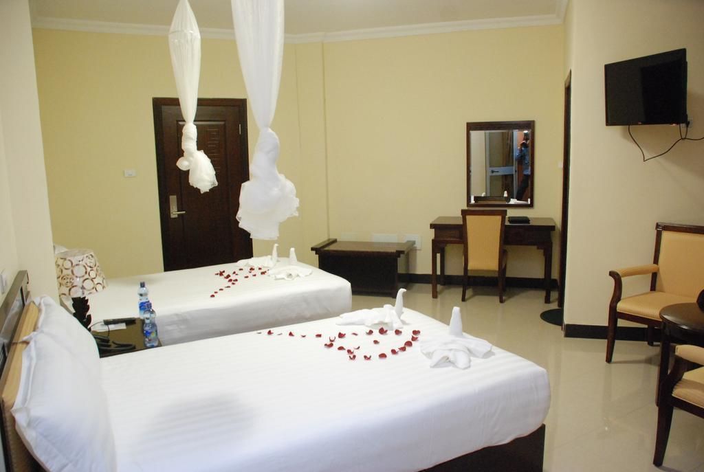 A hotel room with two beds, a desk, a chair, a television, and a mirror.