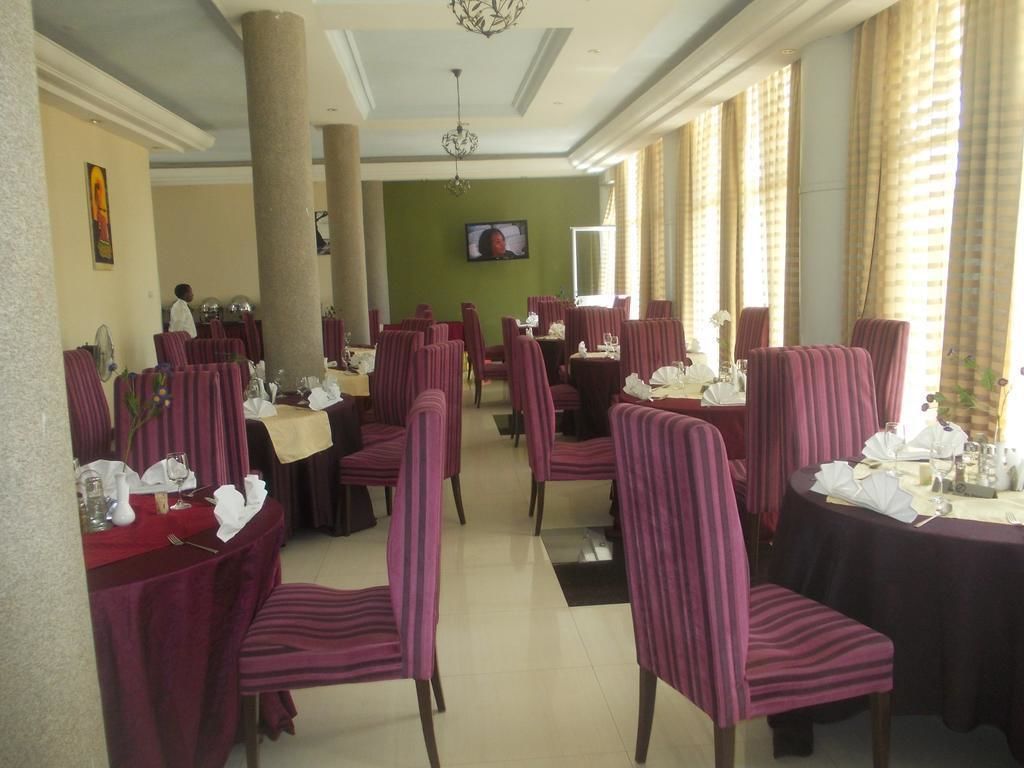 A dining area with multiple tables and chairs, a television screen on the wall, and large windows with curtains.