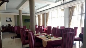 Un comedor con sillas y mesas a rayas, ventanas grandes con cortinas y una araña.