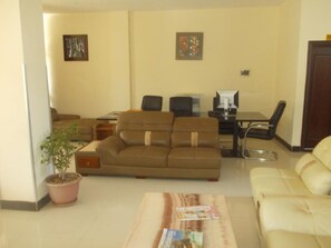 A living room with a sofa, a coffee table with magazines, a potted plant, and a dining area with a table and chairs. - Asinuara Hotel (Bahir Dar)