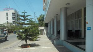 Entrada de un hotel con un corredor cubierto, un árbol pequeño y un coche aparcado.