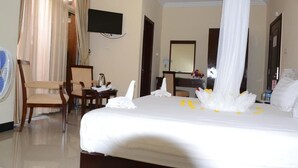 Habitación de hotel con cama, escritorio, silla, televisor y un ventanal con cortinas.