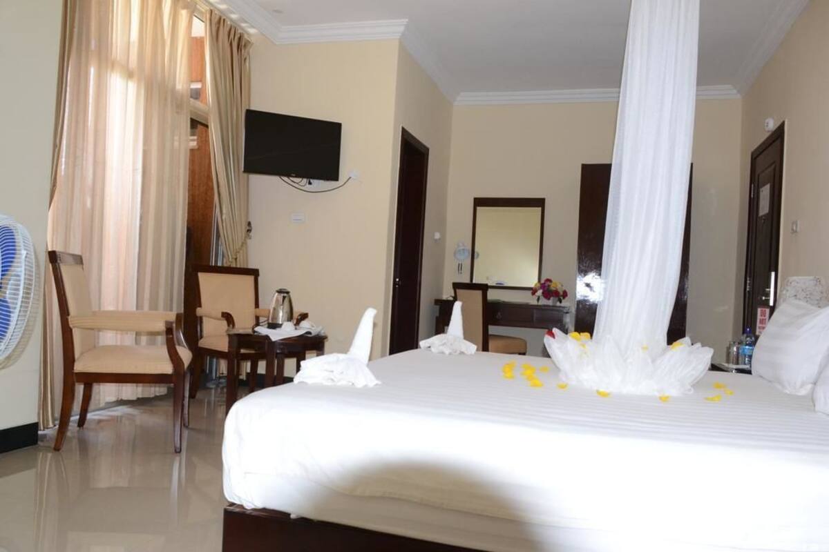A hotel room with a bed, a desk, a chair, a television, and a large window with curtains.