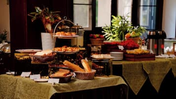 Mesa de buffet com diversos alimentos e uma planta ao fundo.