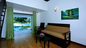 Uma sala de estar moderna com um sofá, uma mesa de centro com flores, uma pintura e vista para uma piscina ao ar livre.