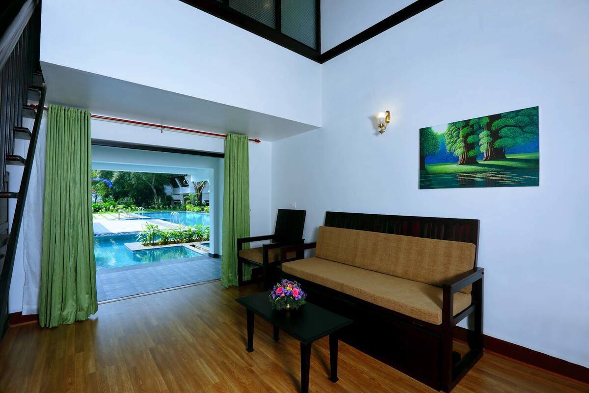 A modern living room with a sofa, a coffee table with flowers, a painting, and a view of an outdoor swimming pool.