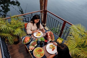 A dining area with a view of water, featuring a table with various dishes and a bottle of red beverage.