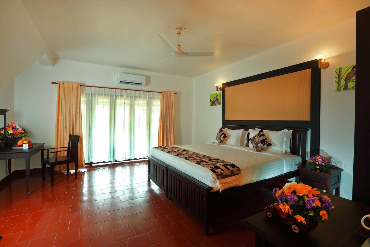 A hotel room with a large bed, a desk with a chair, and a small table with a vase of flowers.