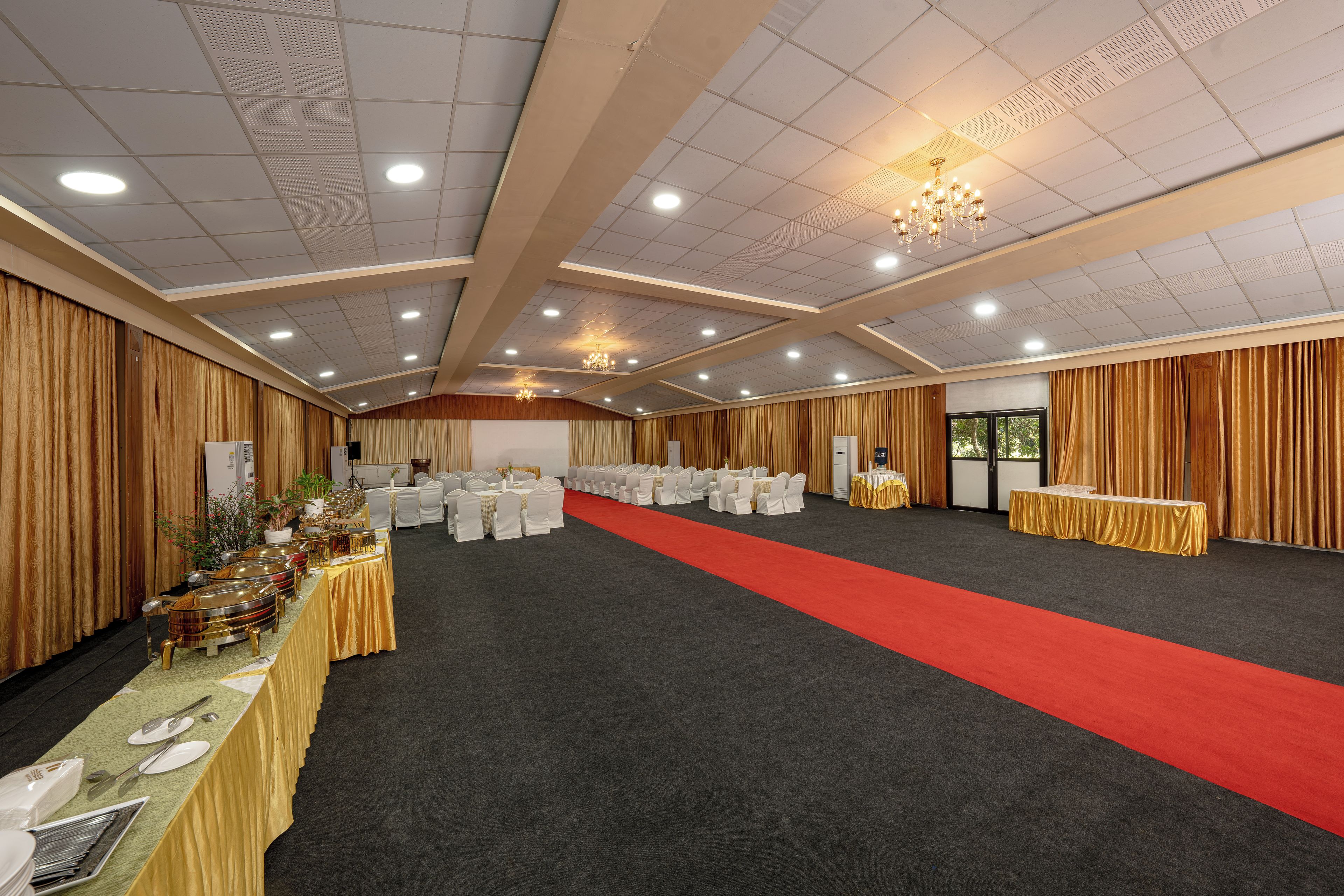 Un salón de banquetes con filas de mesas, una alfombra roja y una araña.