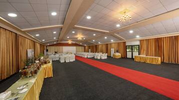 Un salón de banquetes con filas de mesas, una alfombra roja y una araña.