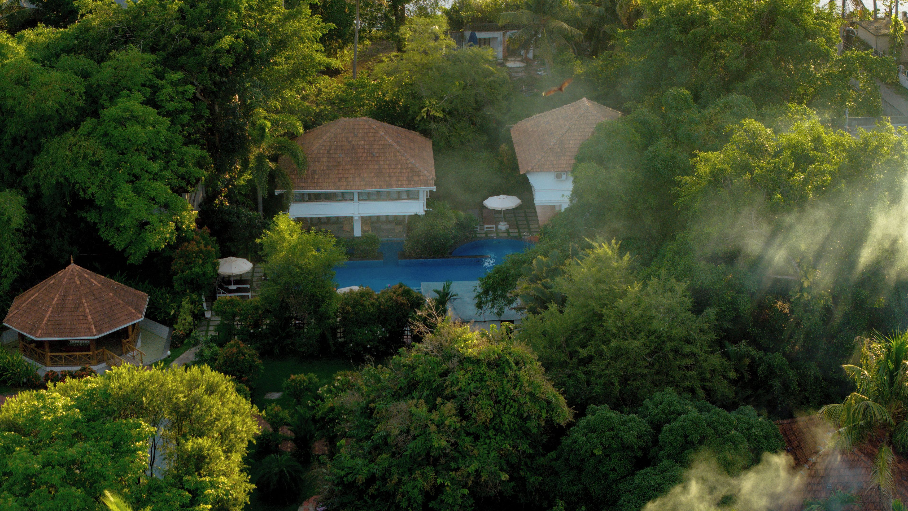 A residential area with a swimming pool surrounded by lush greenery and houses with tiled roofs.
