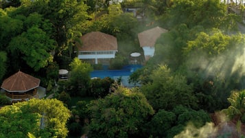 Zona residencial com piscina, cercada por vegetação exuberante e casas com telhados de azulejo.