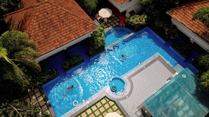 Une vue aérienne d’une piscine dotée de plusieurs couloirs, entourée d’une végétation luxuriante et surmontée d’une structure de toit en tuiles.