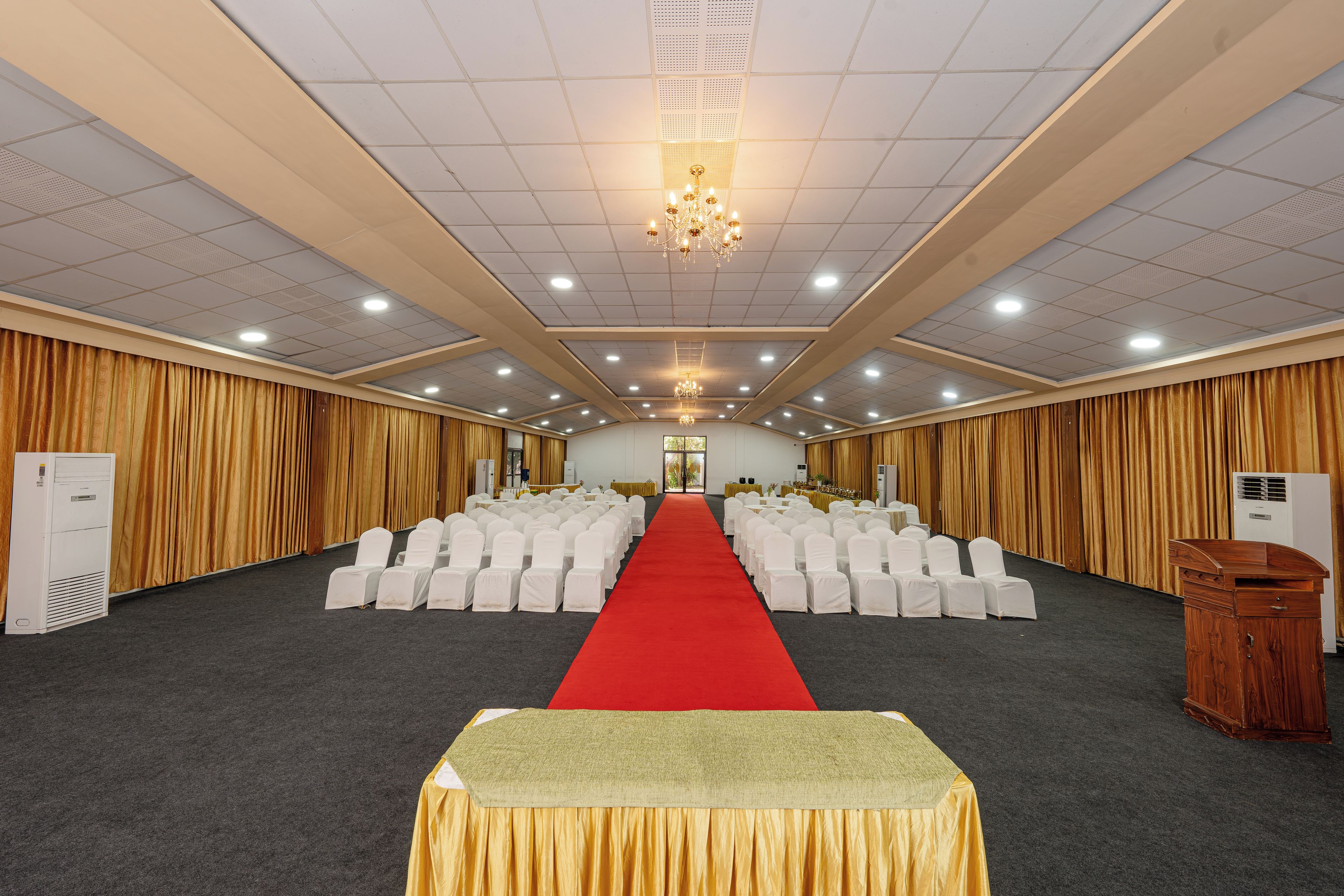A conference room with rows of white chairs, a red carpet, and a chandelier.
