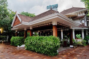 A traditional building with a tiled roof, a covered entrance area, and lush greenery.