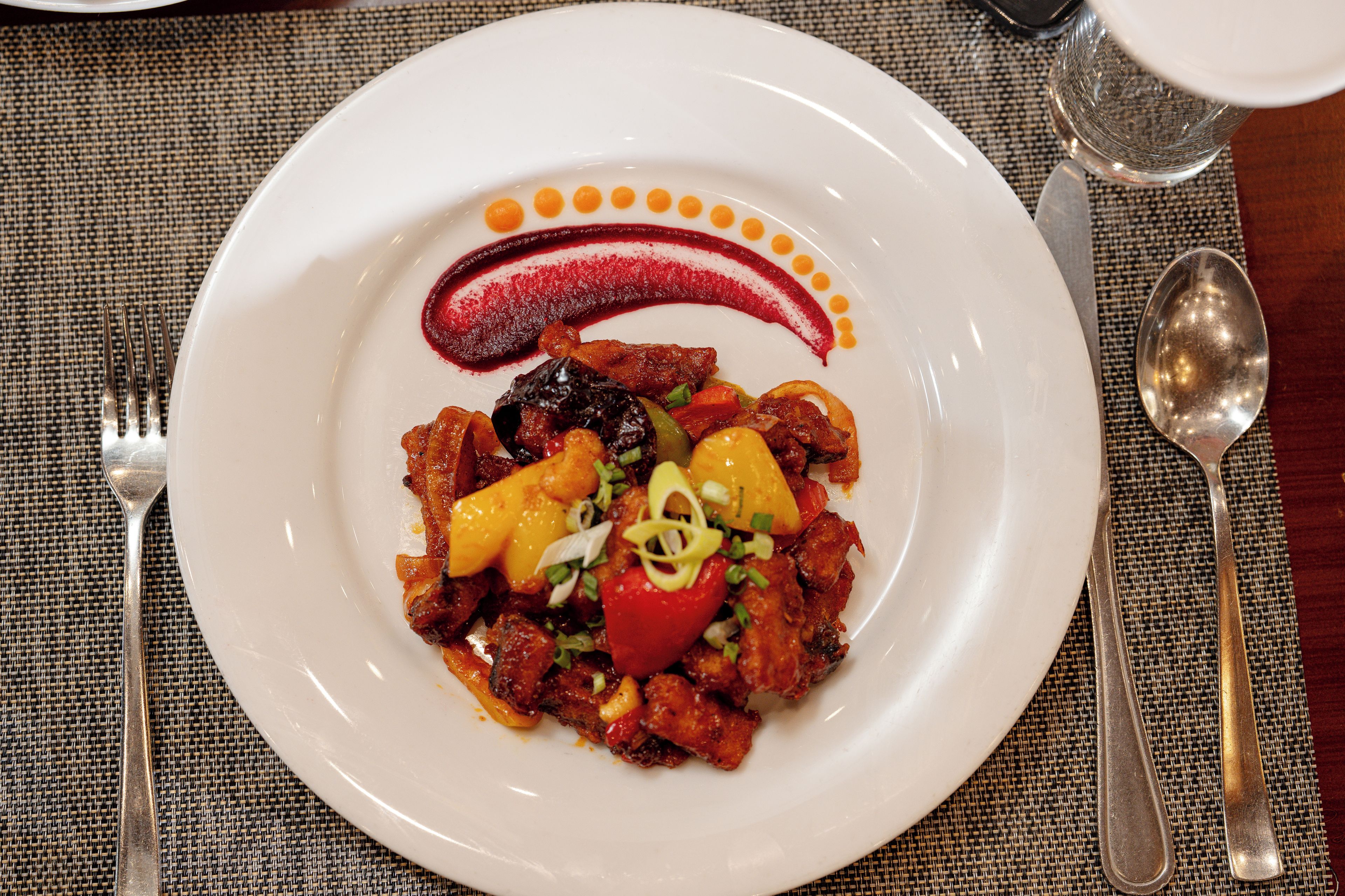 A plate of food with a decorative sauce design, accompanied by cutlery on a woven tablecloth.