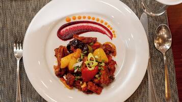 A plate of food with a decorative sauce design, accompanied by cutlery on a woven tablecloth.