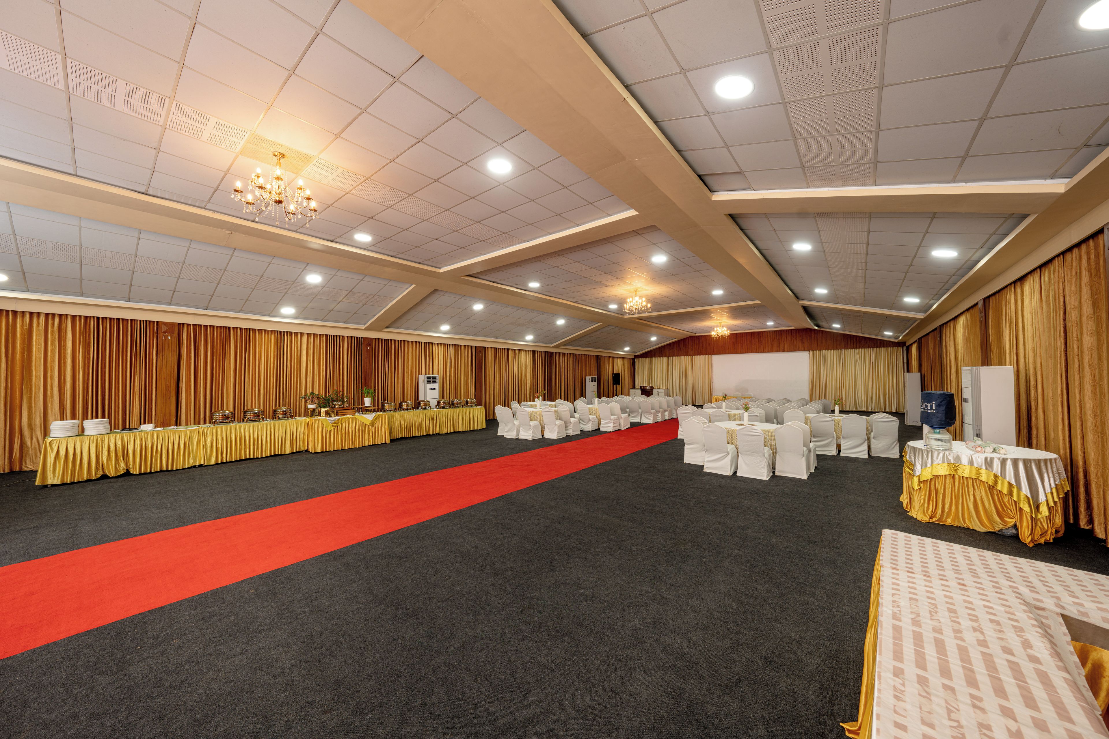 A banquet hall with a red carpet, tables with white chairs, and a stage area.