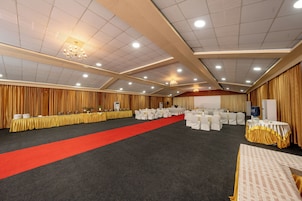 Une salle de banquet avec un tapis rouge, des tables entourées de chaises blanches et une scène.