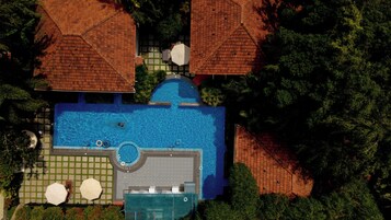 Vue aérienne d’un complexe hôtelier doté d’une piscine centrale, de plusieurs structures abritées et d’une végétation luxuriante.