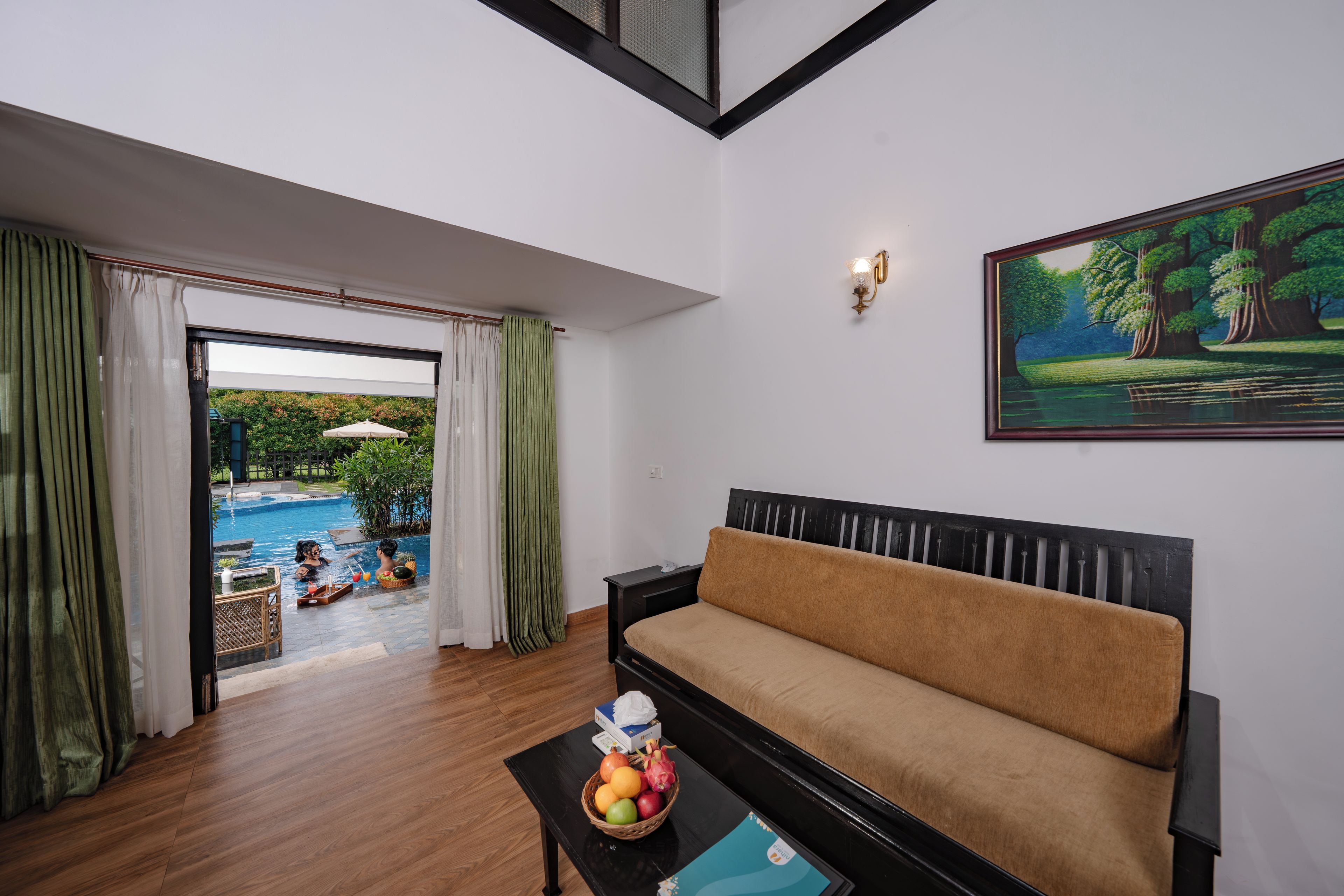 Una habitación con sofá, una mesa con fruta, un cuadro y vista a una piscina.