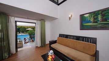 Una habitación con sofá, una mesa con fruta, un cuadro y vista a una piscina.
