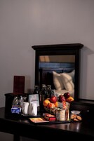 Habitación de hotel con una mesa de comedor dispuesta con diversos alimentos, una cafetera y un espejo que refleja la habitación.