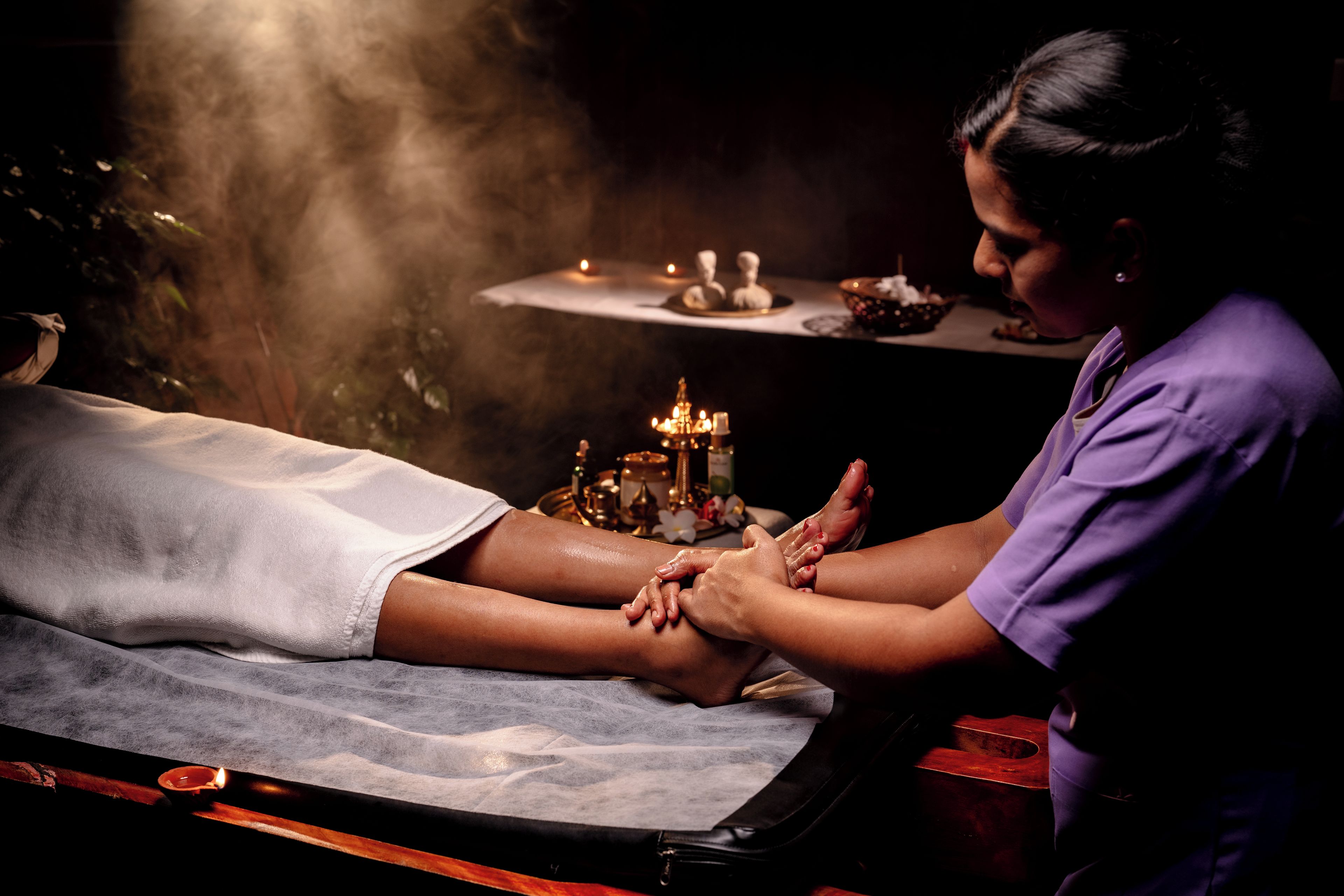 Uma pessoa recebendo massagem nos pés, com velas e um pequeno altar ao fundo.