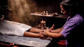 Uma pessoa recebendo massagem nos pés, com velas e um pequeno altar ao fundo.
