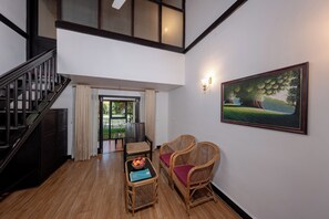 A spacious room with a staircase, a dining area with wicker furniture, and a painting on the wall. - Nihara Resort And Spa (Kanayannur)