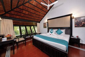 A hotel room with a bed, a desk, a chair, a window with curtains, a ceiling fan, and a painting on the wall.