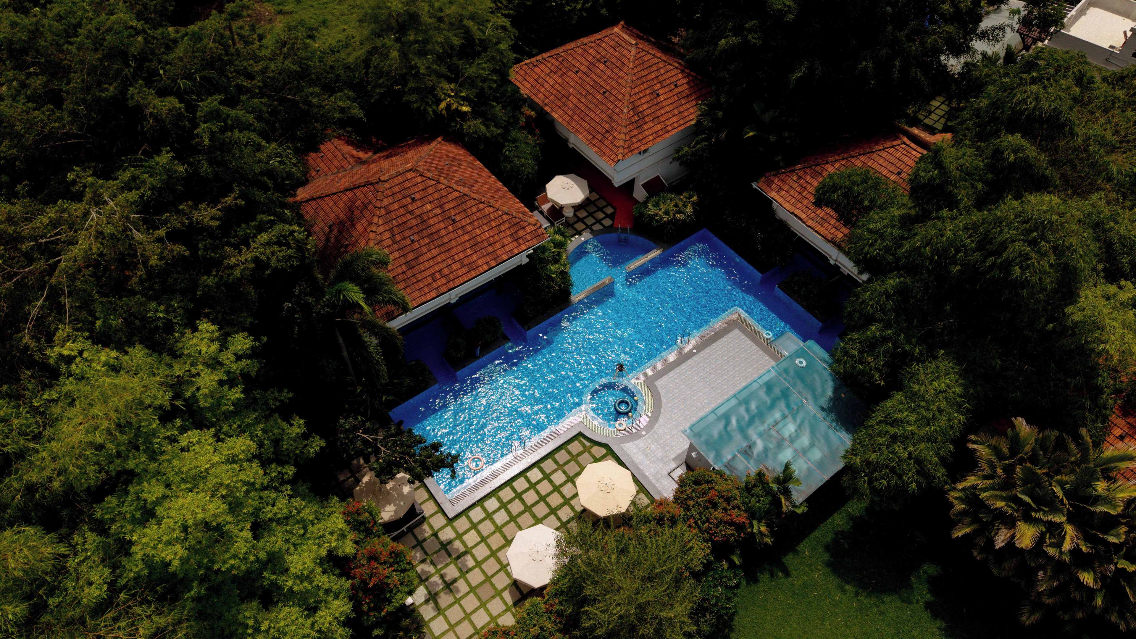 Vista aérea de una propiedad con piscina rodeada de abundante vegetación y una casa con techo de tejas rojas.