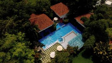 Vista aérea de una propiedad con piscina rodeada de abundante vegetación y una casa con techo de tejas rojas.