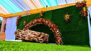 Ein Zelt mit grünem Kunstgrase, einem floralen Bogen und einer hölzernen Bank.
